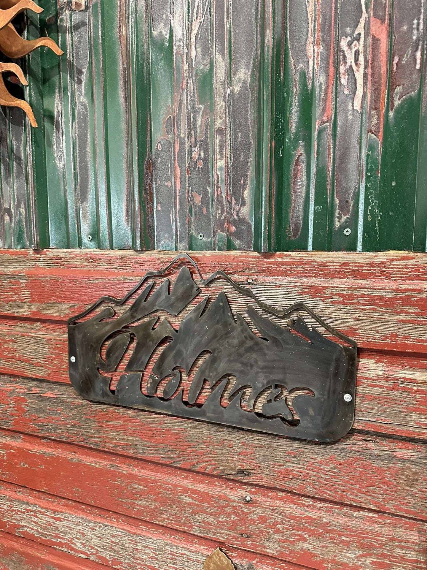 Steel mountain silhouette sign with script family name mounted on weathered red siding