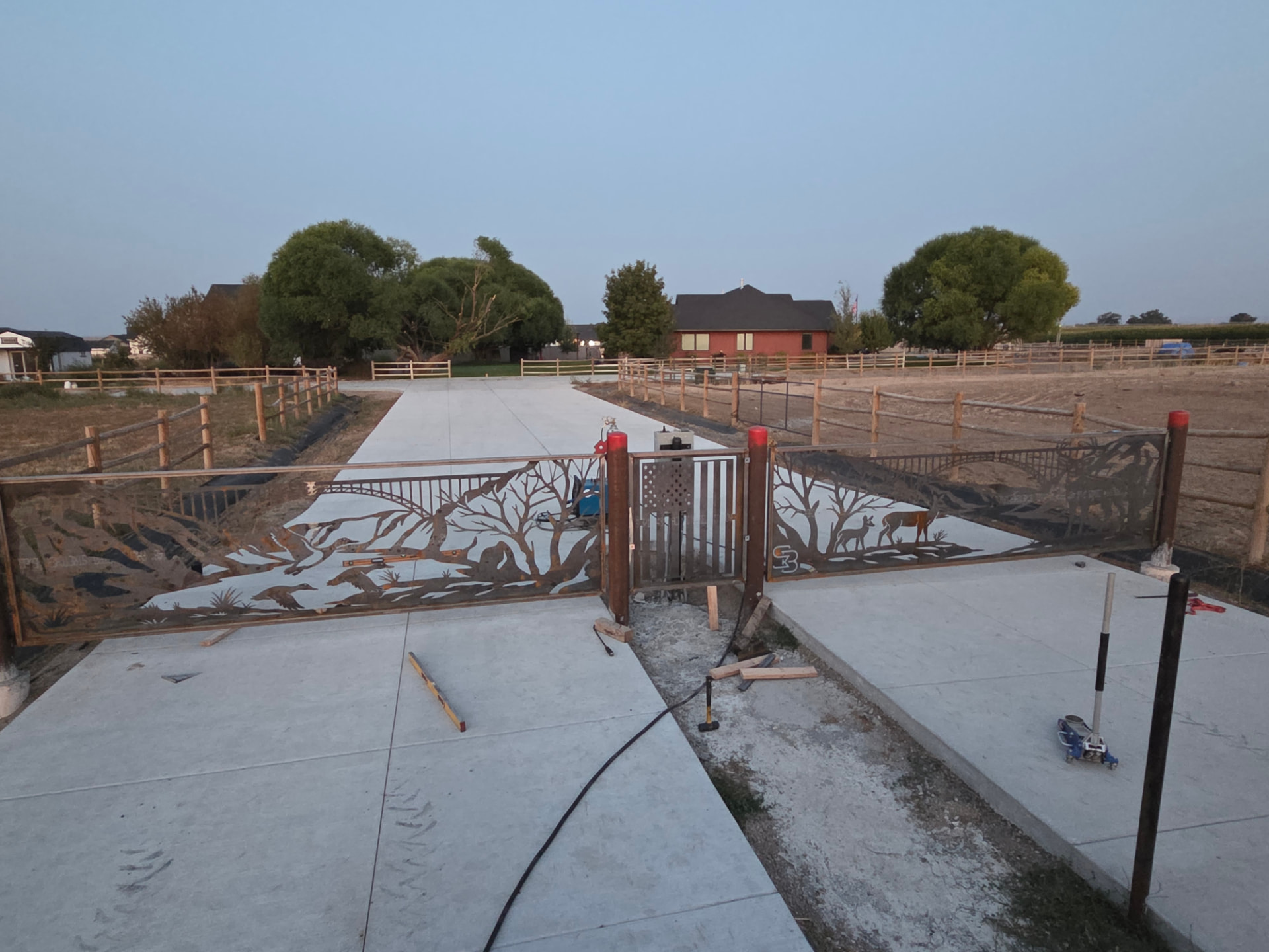 Dual swinging driveway gates with CNC-cut wildlife, tree and mountain scene panels