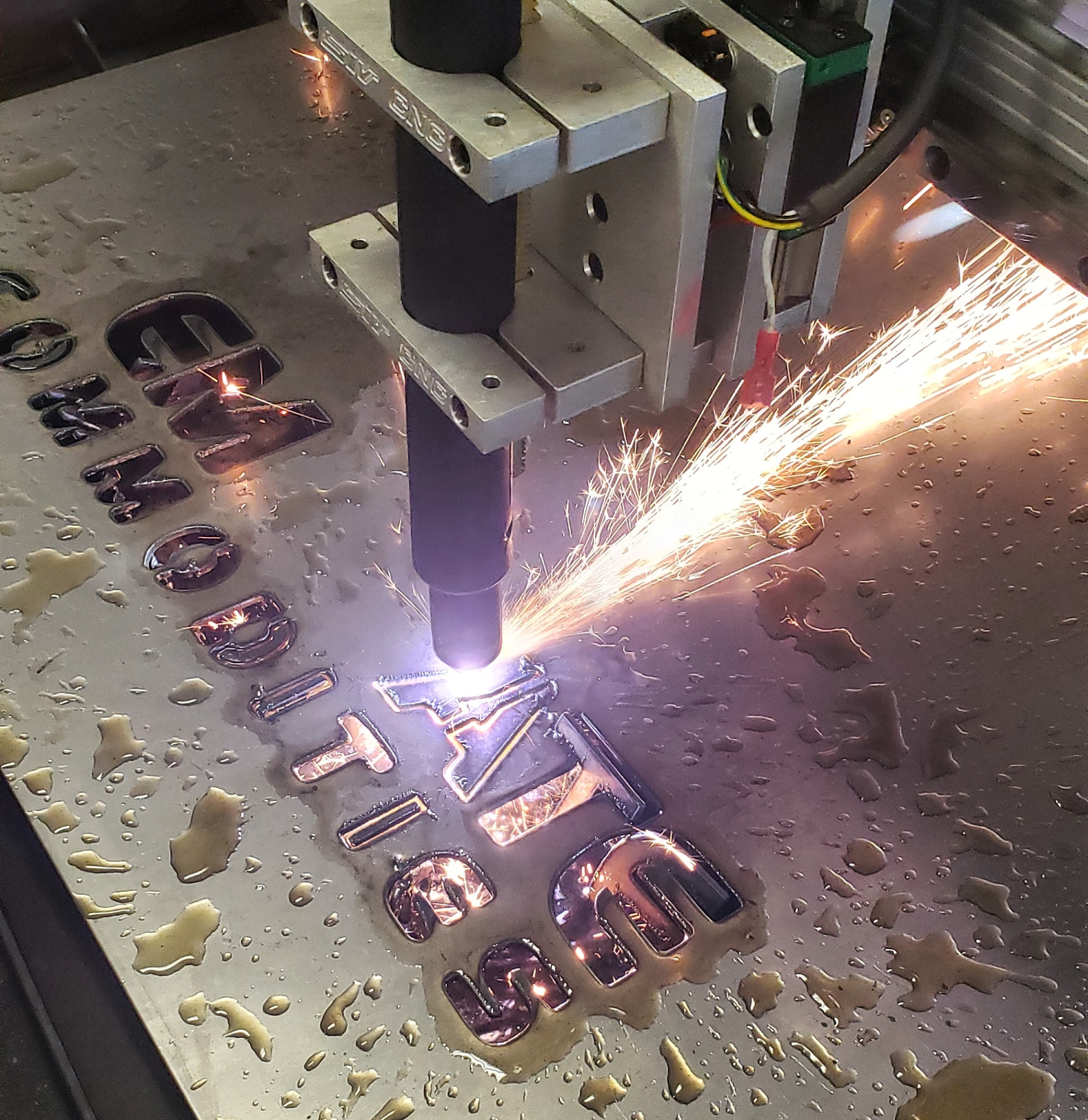CNC plasma torch cutting steel letters on a water table with sparks