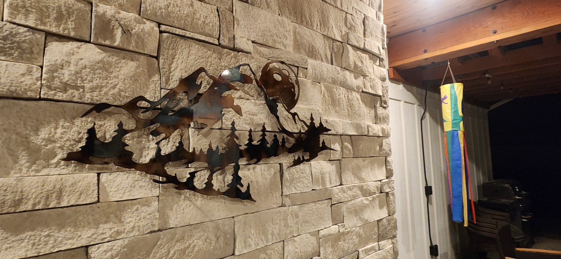 Torch finished steel mountain and pine tree wall art mounted on a stone wall