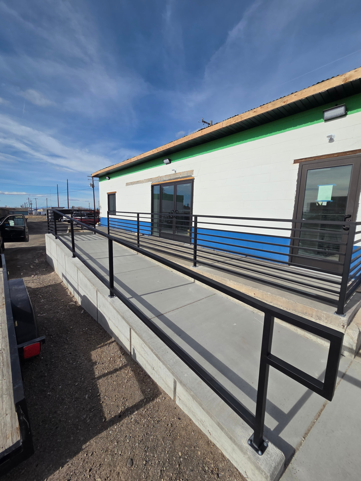 Black steel ADA ramp railing with horizontal bars along a concrete ramp outside a commercial building