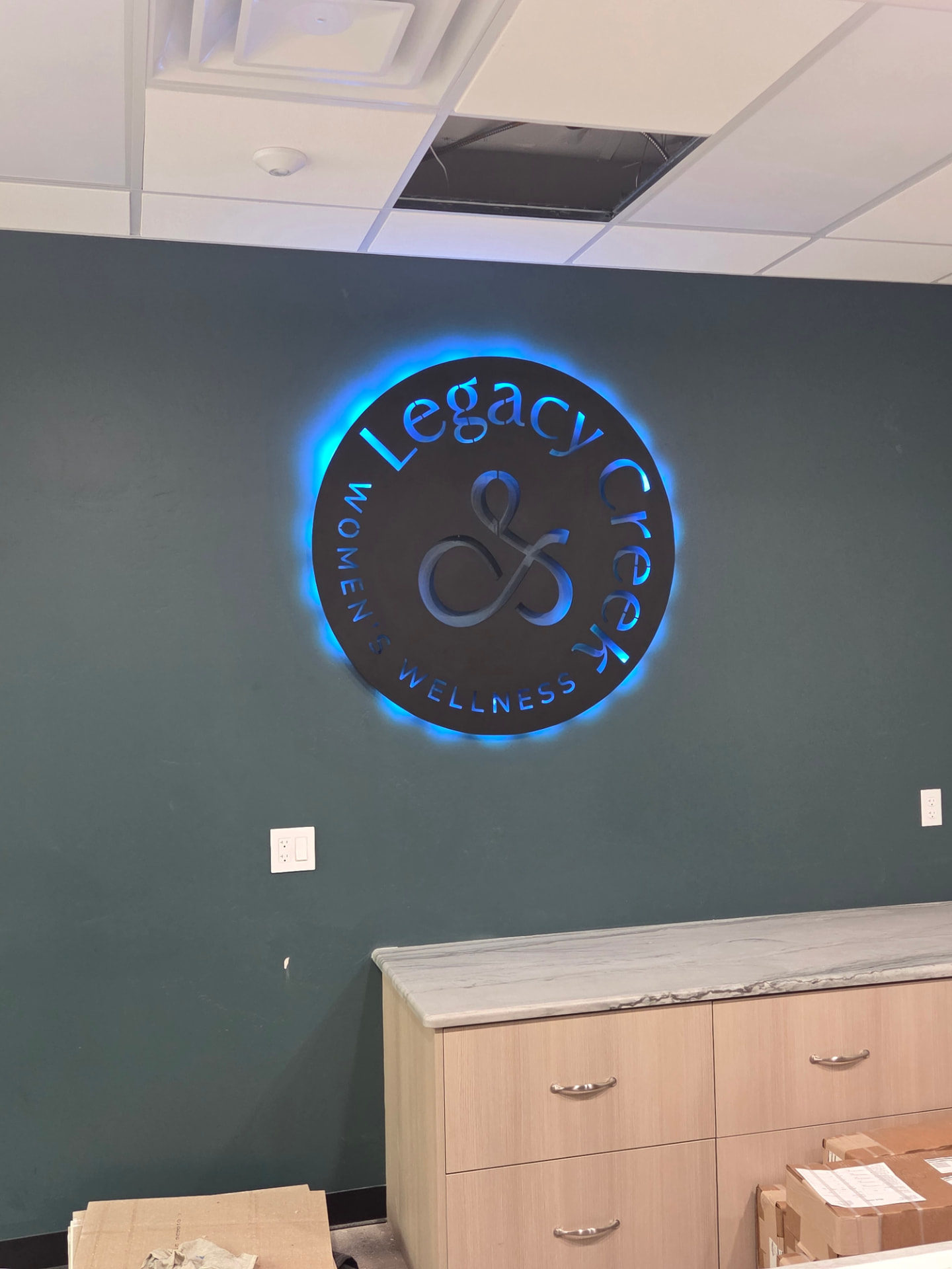 Round backlit metal business logo sign with blue LED halo lighting on an interior wall
