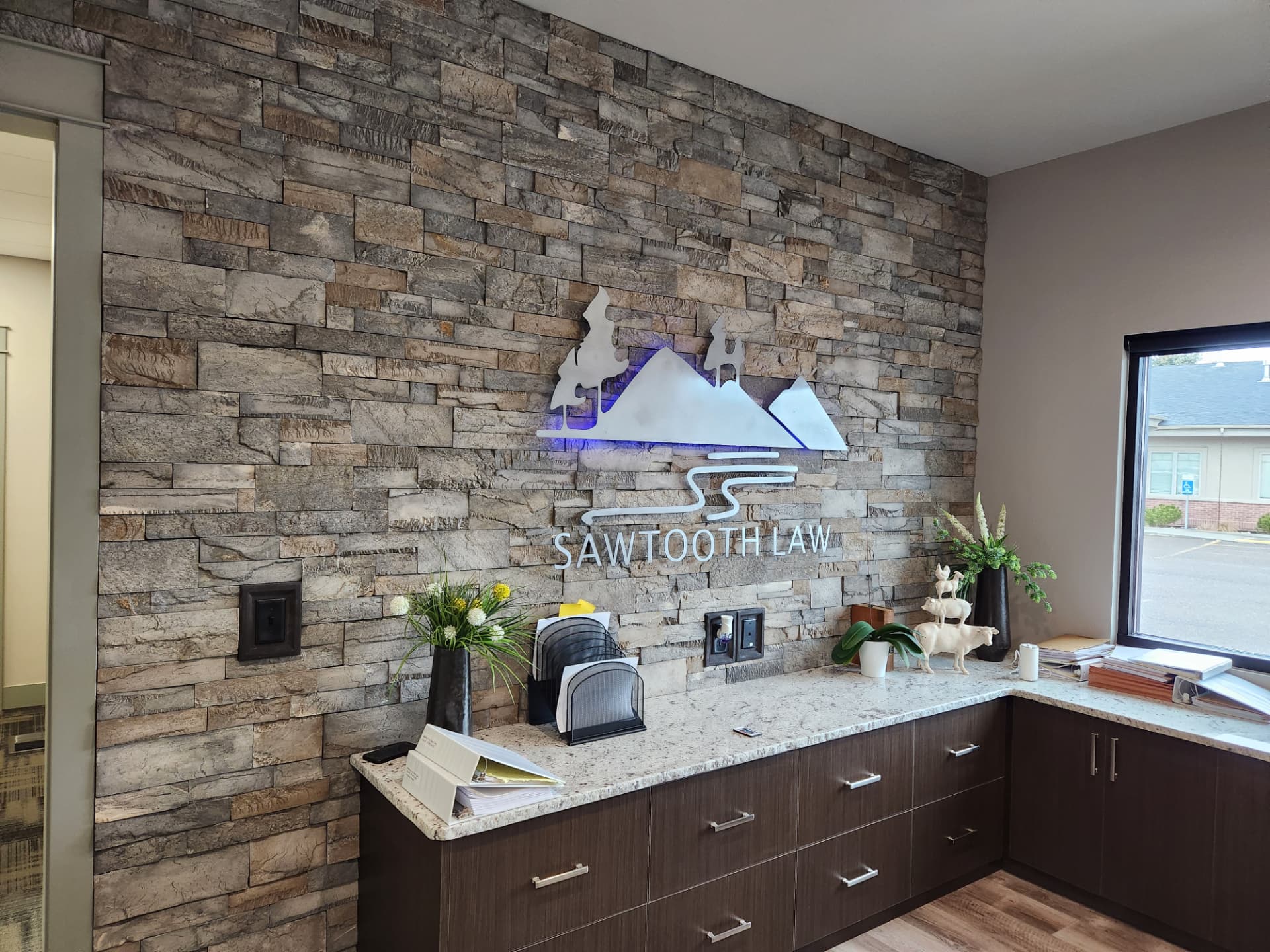 Brushed metal mountain logo sign with LED backlighting on a stone lobby wall