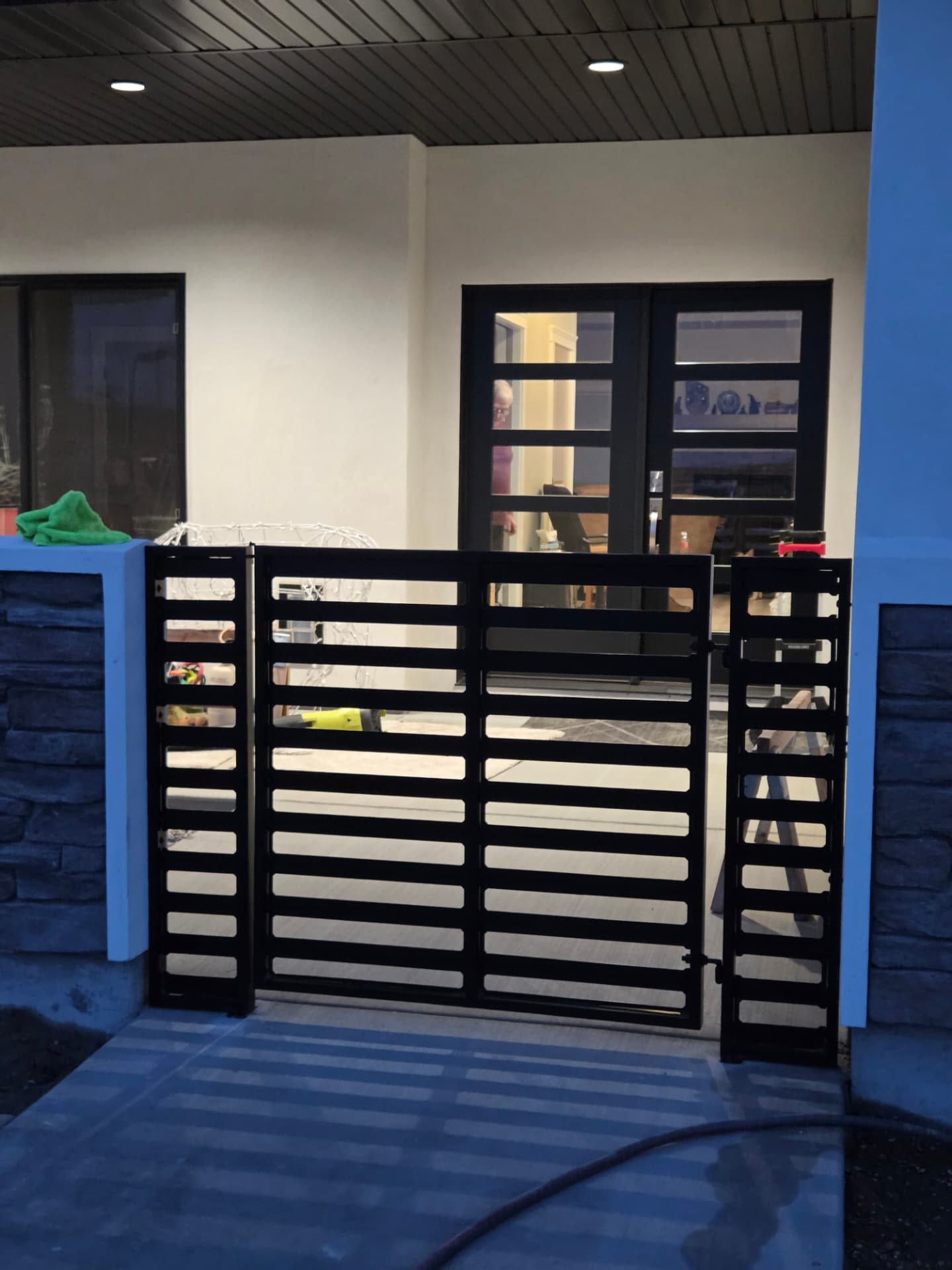 Black horizontal slat steel courtyard gate with side panels at dusk