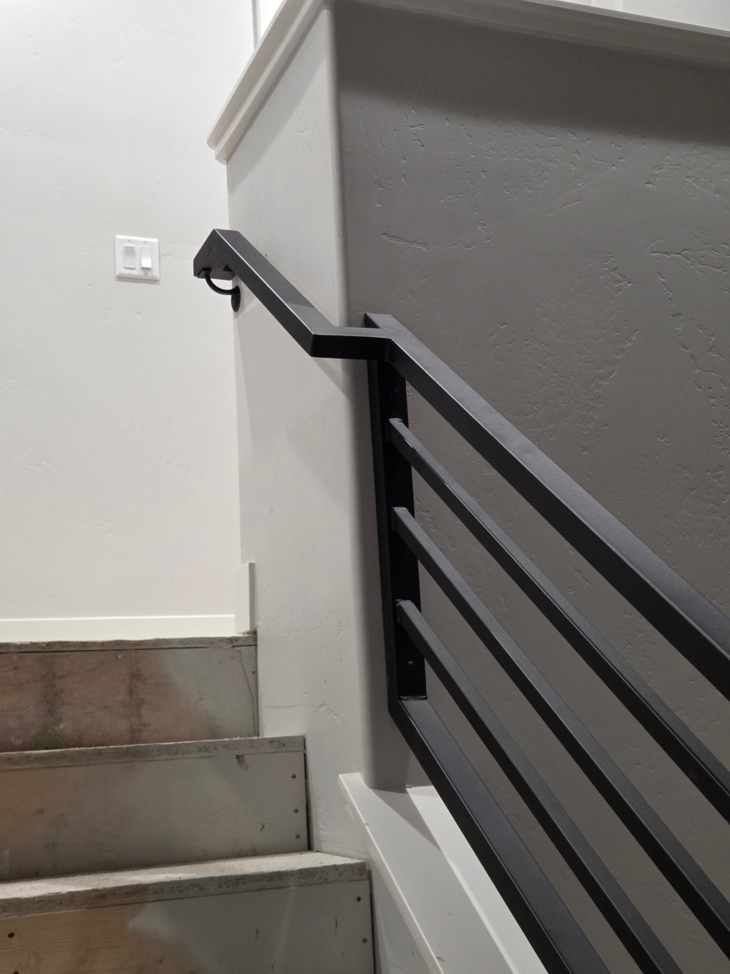 Black steel horizontal bar stair railing mounted along a painted interior wall with concrete steps